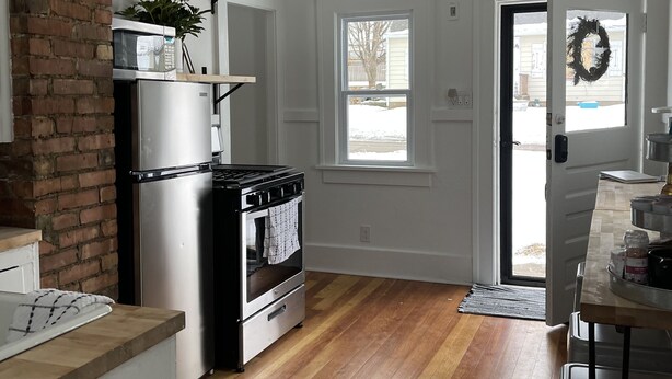 A kitchen with a brick wall, stainless steel appliances, a wooden floor, and a view of the outside through a door. - Cozy Cottage located near Czech Village and Newbo areas in Cedar Rapids, IA (Cedar Rapids)
