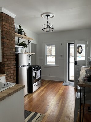 A kitchen with a brick wall, stainless steel appliances, a wooden floor, and a view of the outside through a door. - Cozy Cottage located near Czech Village and Newbo areas in Cedar Rapids, IA (Cedar Rapids)
