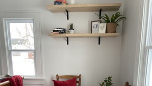 A room with wooden flooring, two wooden chairs with cushions, a bookshelf, and a window with a view. - Cozy Cottage located near Czech Village and Newbo areas in Cedar Rapids, IA (Cedar Rapids)