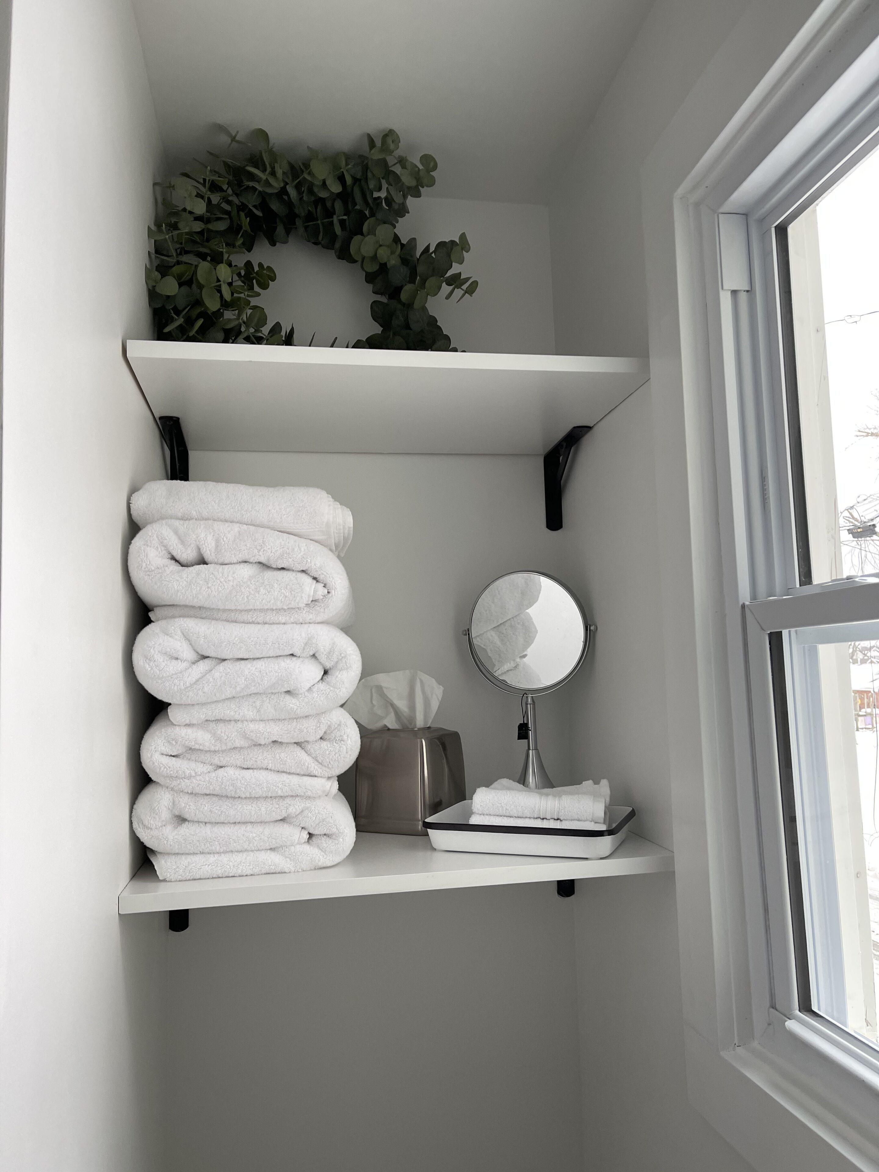 Un baño con estantes blancos que sostienen toallas, una caja de pañuelos y un espejo.