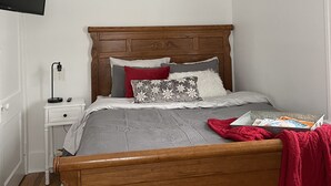A neatly arranged bedroom with a wooden bed, a bedside table with a lamp, and a wall-mounted TV. - Cozy Cottage located near Czech Village and Newbo areas in Cedar Rapids, IA (Cedar Rapids)