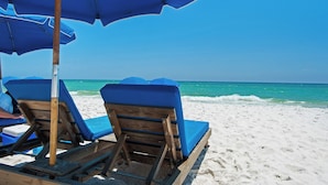 A beach with wooden lounge chairs and blue umbrellas.
