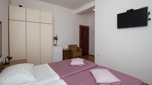 A hotel room with a bed, a wardrobe, a desk with a lamp, a chair, and a TV mounted on the wall.