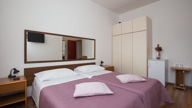 A hotel room with a large bed, a wardrobe, a desk, a mirror, and a small refrigerator.