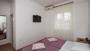 A hotel room with two beds, a TV, an air conditioner, and a window with sheer curtains.