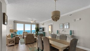 A spacious living area with a large dining table, comfortable seating, and a view of the ocean.