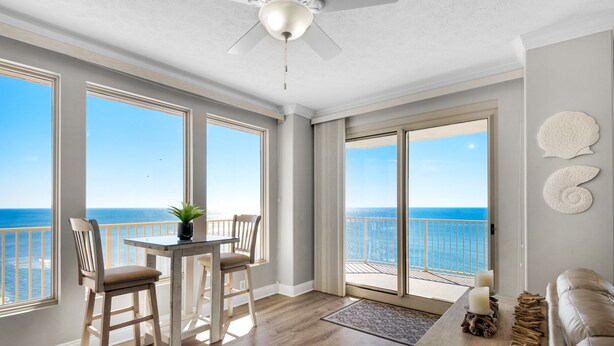 A spacious room with large windows offering a view of the ocean, a ceiling fan, and a wooden floor.