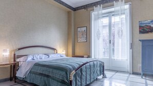 Een slaapkamer met een bed, nachtkastje, stoel, deur en een schilderij aan de muur.