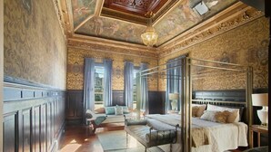 A luxurious bedroom with a four-poster bed, a chaise lounge, and a large window with curtains.