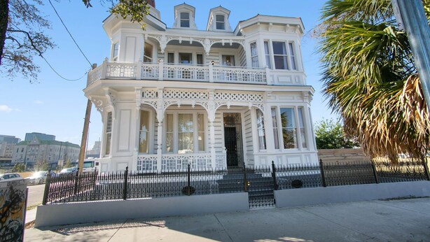 A Victorian-style building with a balcony, large windows, and a white facade.
