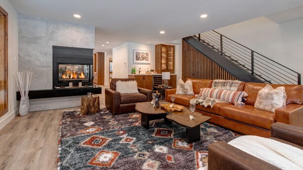Una sala de estar moderna con chimenea, una escalera y una cocina al fondo.