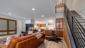 Un salón moderno con un sofá de cuero, una escalera y una cocina al fondo.