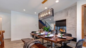 Un comedor con una mesa de madera preparada para cuatro personas, un banco y una escalera que sube a un nivel superior.