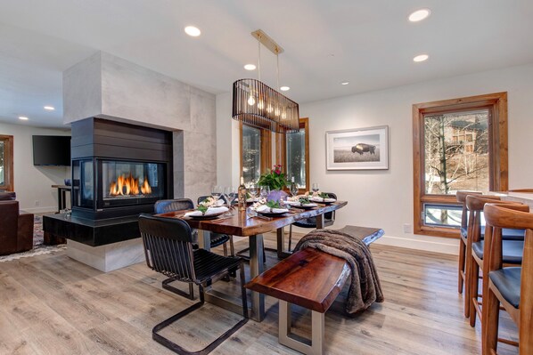 A modern living room with a fireplace, dining area, and large windows.