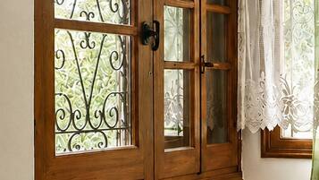 A wooden door with glass panels and a decorative iron gate, a wicker lamp, and a window with a white curtain.