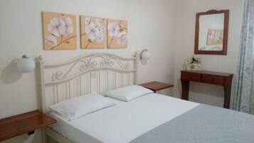 A bedroom with a white bed, a wooden nightstand, a bedside table, and a mirror on the wall.