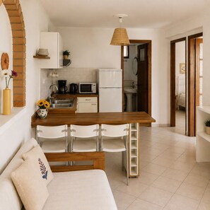 Une cuisine moderne avec des meubles blancs, une table à manger en bois et un canapé blanc agrémenté d’un coussin décoratif.