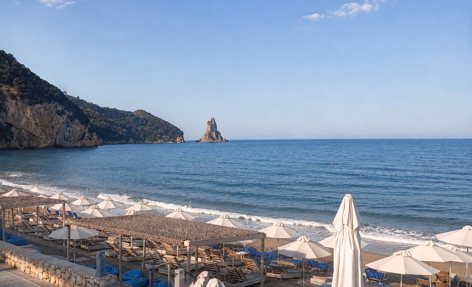 A beach with umbrellas and lounge chairs, a rocky coastline, and a distant island.