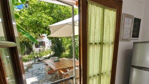 A kitchen with a refrigerator, a dining table, and a view of a garden through a glass door. - Cottage House (Agios Gordios, Corfu)