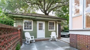 Una casita con fachada verde, una puerta blanca y dos sillas blancas en el exterior.