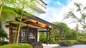 A modern building with a covered entrance, large windows, and a garden with rocks and greenery. -  Livemax Resort Izukogen ANNEX (Ito)