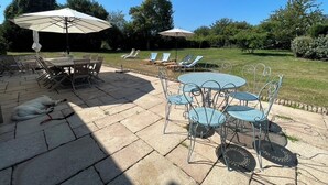 Un patio al aire libre con mesas y sillas de metal, rodeado de césped y árboles.