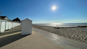 Una playa con un paseo de madera, cabañas de playa y un cielo despejado.