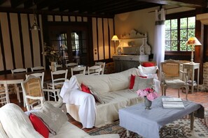 Una habitación acogedora con un conjunto de sofás, una mesa de comedor y sillas, una lámpara y un florero con flores.
