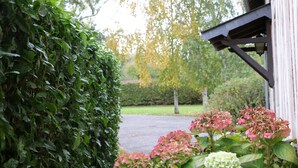 Un jardín con seto, flores de hortensia rosas y un edificio blanco con estructura de madera.