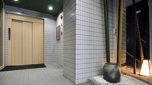Un couloir aux murs recouverts de carreaux, une porte en bois et une plante en pot.