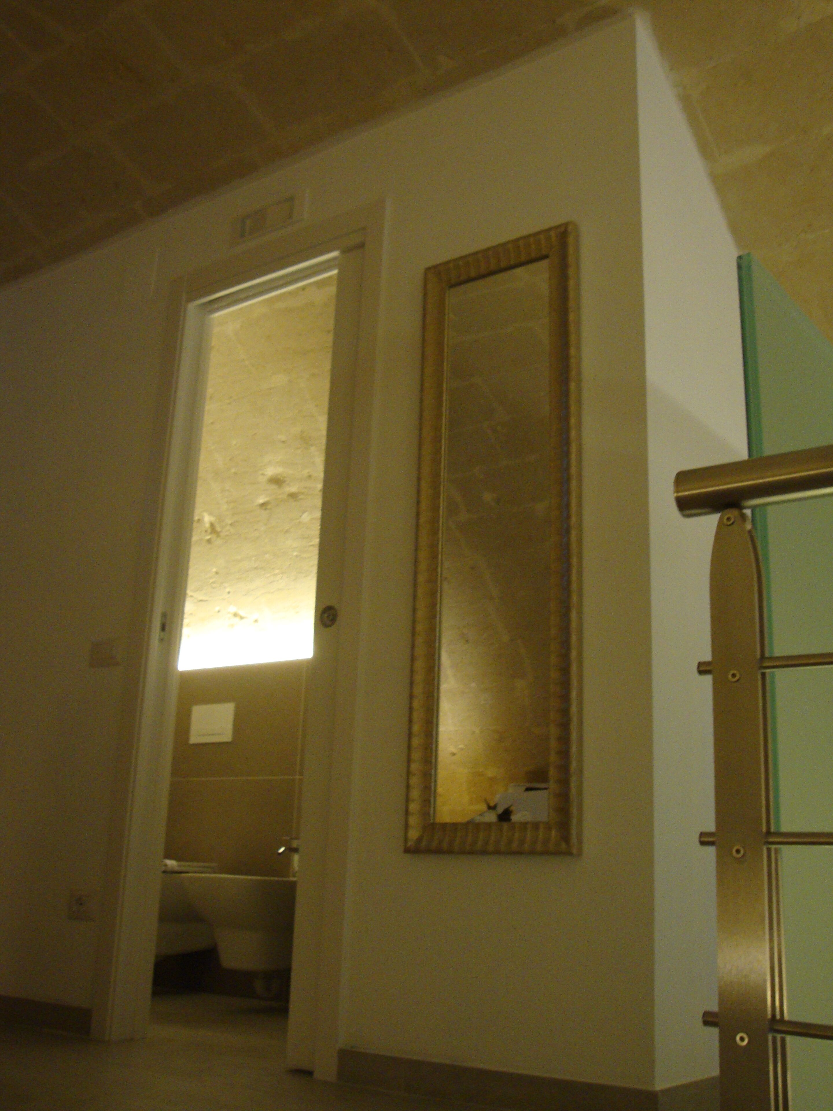 A bathroom with a toilet, a mirror, and a door leading to another room.