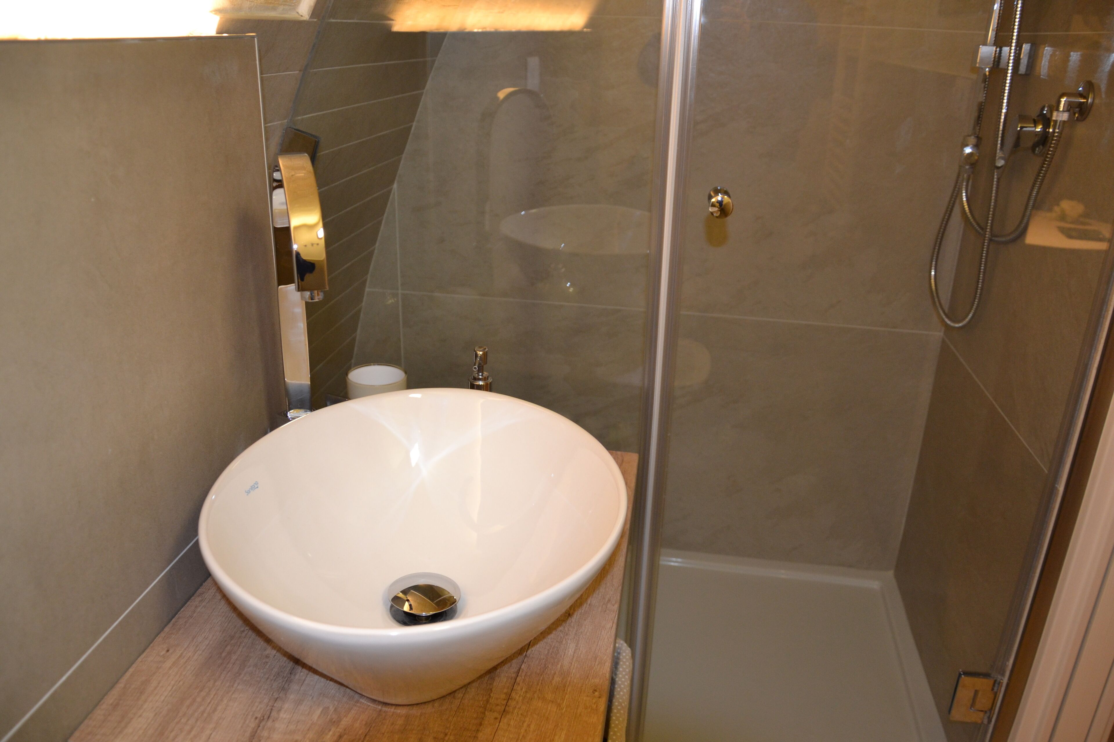 Ein modernes Badezimmer mit einem großen, weißen Waschbecken, einer Duschkabine aus Glas und einem hölzernen Waschtisch.