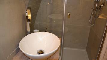 Ein modernes Badezimmer mit einem großen, weißen Waschbecken, einer Duschkabine aus Glas und einem hölzernen Waschtisch.