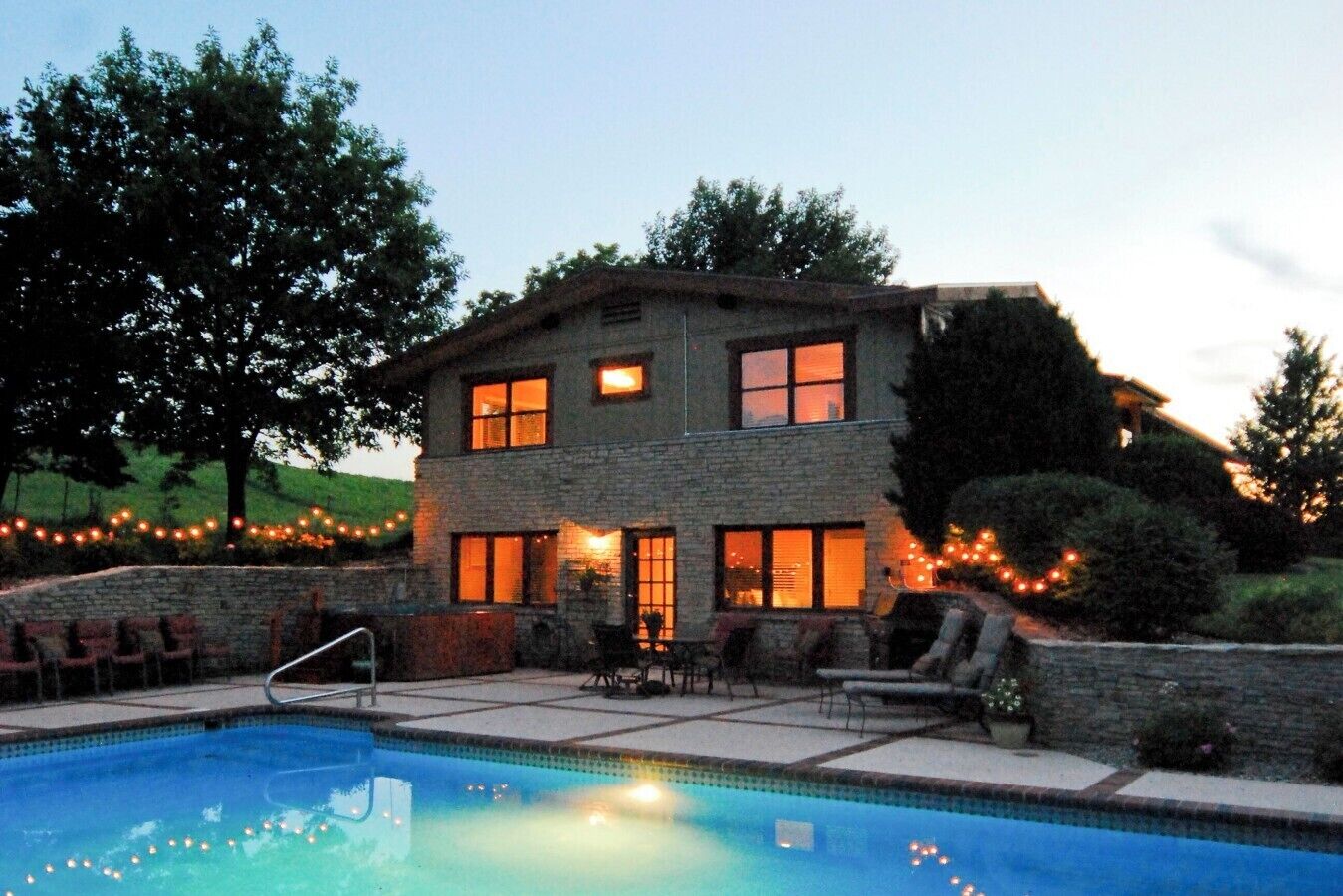 A two-story house with a swimming pool, outdoor seating, and string lights.