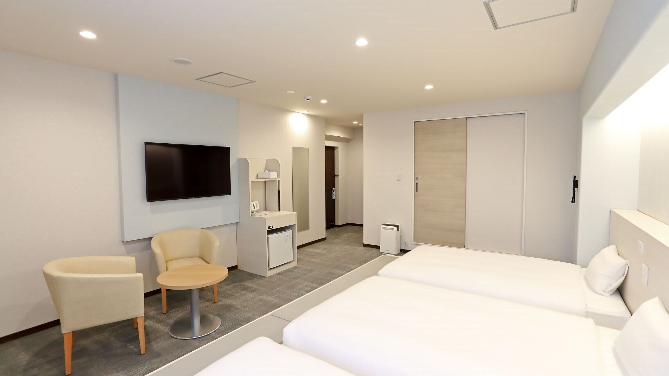 A modern hotel room with two beds, a TV, a desk, a chair, and a wardrobe.