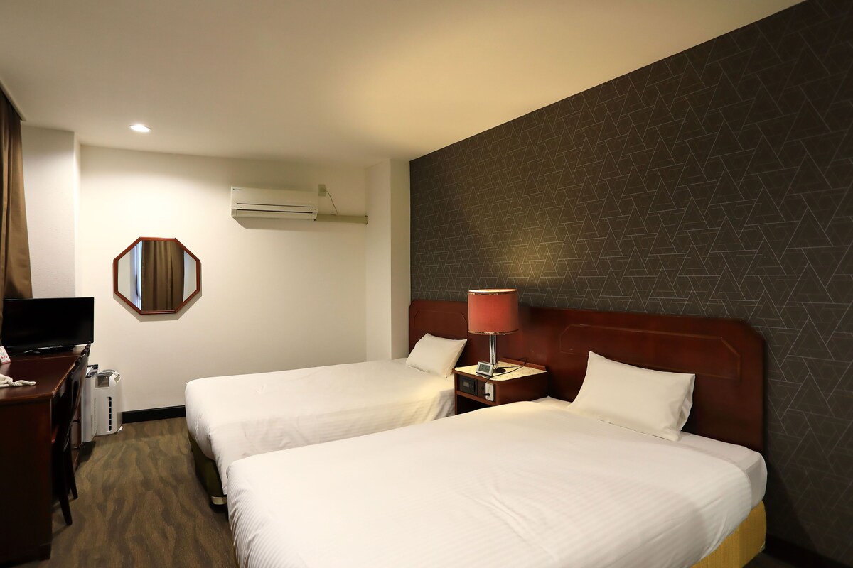 Een hotelkamer met twee bedden, een bureau met een televisie en een wandairconditioner.