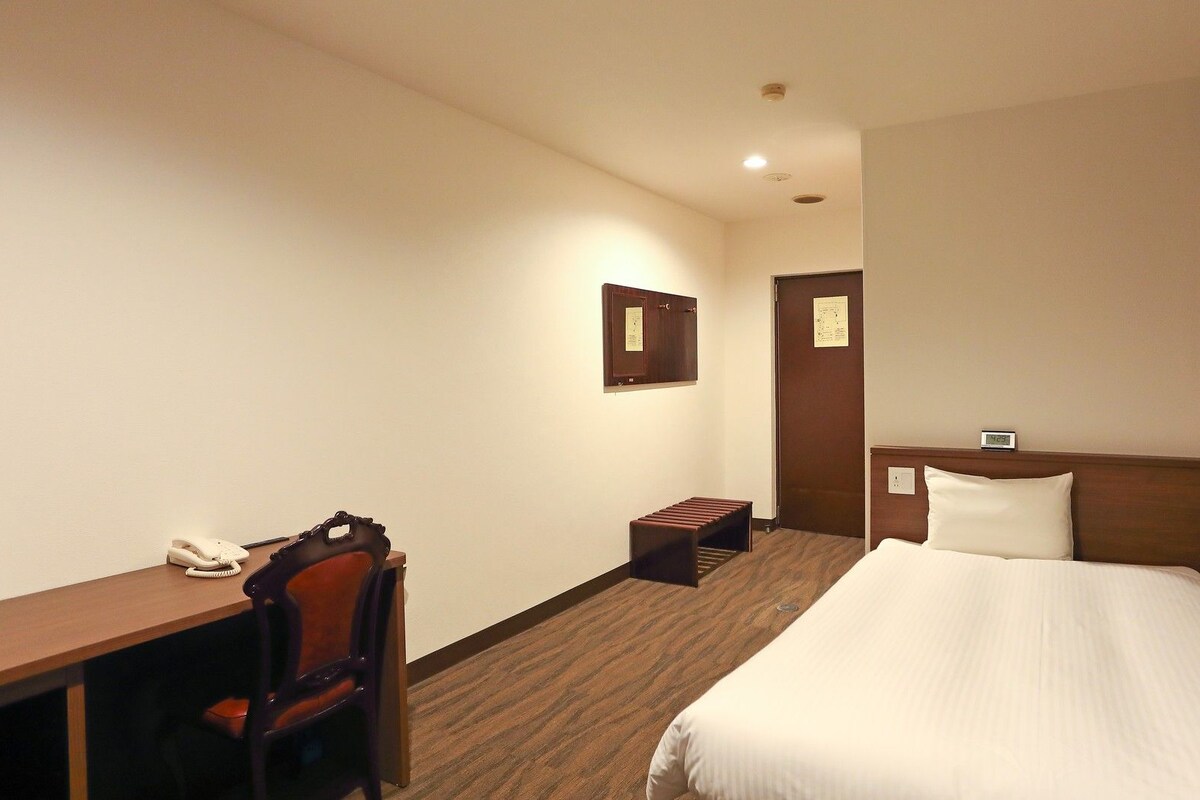 Hotelkamer met een bed, een bureau met telefoon, een stoel, een tafeltje en een wandkast.