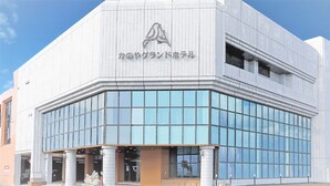 A modern building with a glass facade and a logo at the top. - Kanoya Daikoku Grand Hotel (Kanoya)
