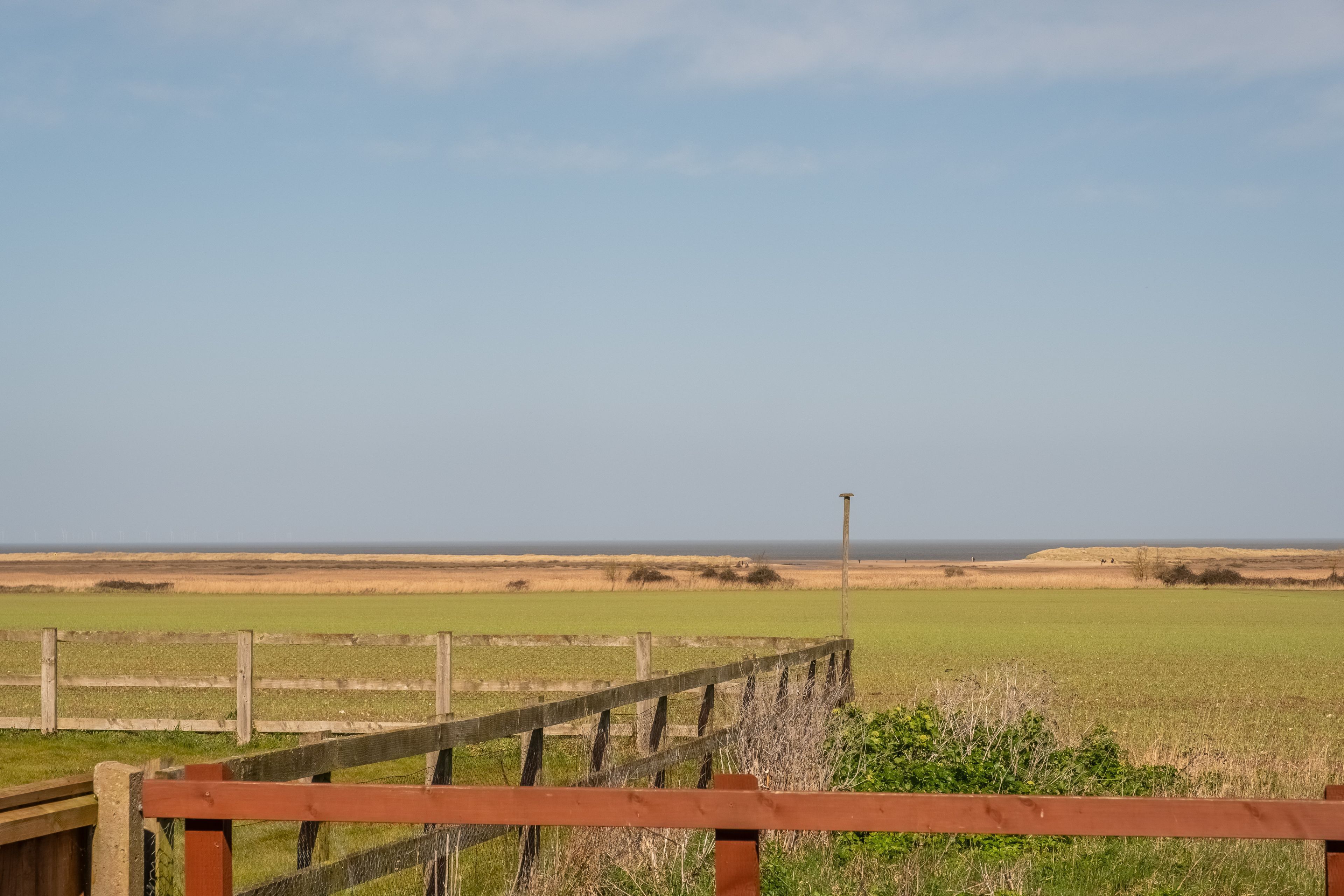 A wooden fence with a view of a green field and a clear sky.