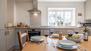 A modern kitchen with a dining table set for two, featuring wine glasses, a bowl of fruit, and a bottle of wine. - Twitchers Cottage, Titchwell, Norfolk (Titchwell)