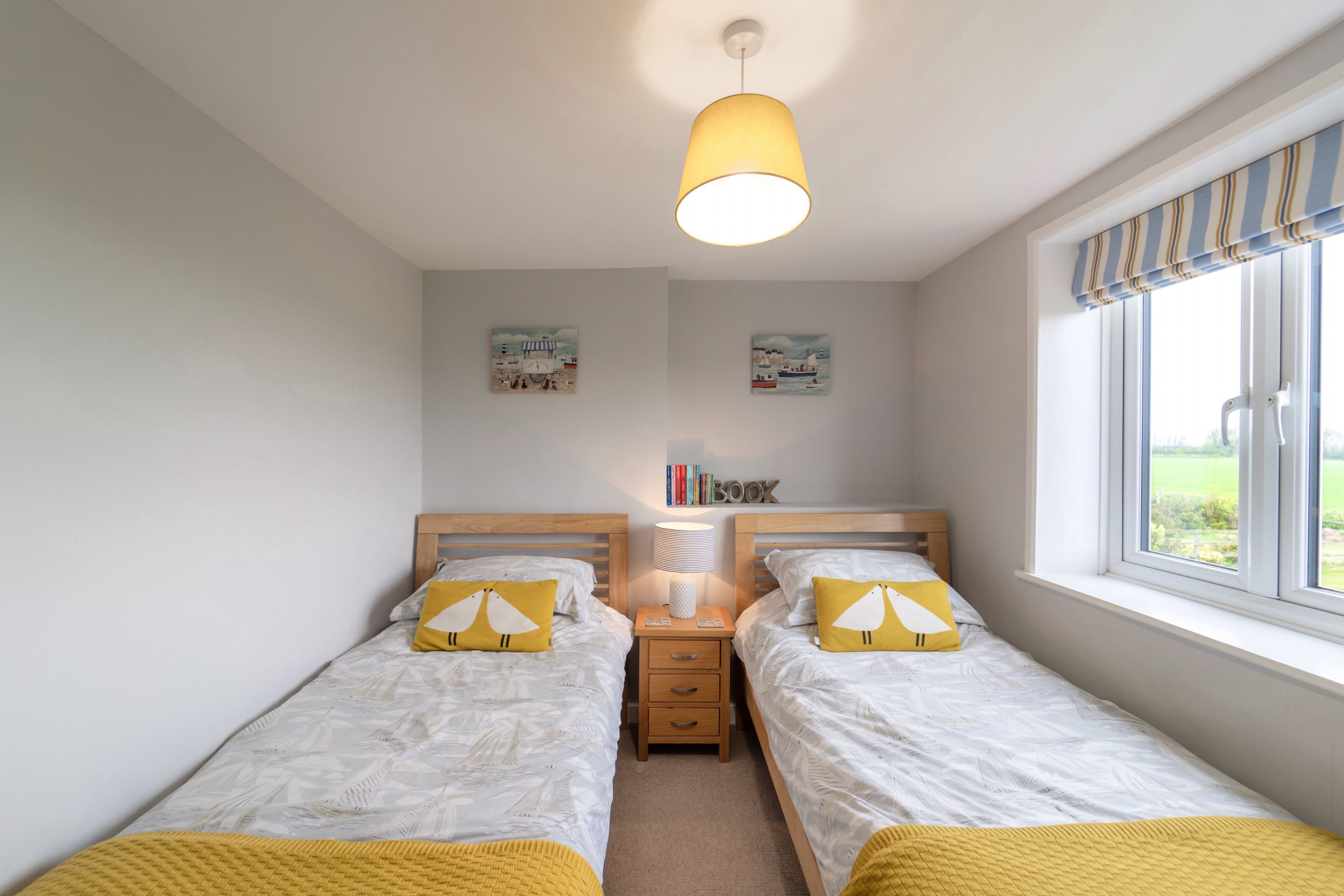 A bedroom with two beds, a nightstand with a lamp, and a window with a view of the outdoors.