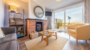 A cozy living room with a fireplace, a sofa, a coffee table, and a balcony with a view. - Twitchers Cottage, Titchwell, Norfolk (Titchwell)
