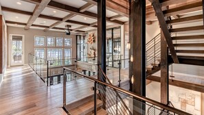 A spacious interior with a wooden floor, a glass railing staircase, and large windows allowing natural light. - Vermillion Sunsets | Lakefront Architectural Gem-Pool/Hot Tub/New 6 Seat LSV (Santa Rosa Beach)