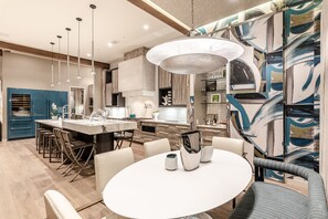 Una cocina moderna con una isla central, iluminación colgante y un comedor con una mesa redonda y sillas.