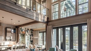 A spacious living area with a large sectional sofa, a coffee table, and a dining area with a kitchen in the background. - Vermillion Sunsets | Lakefront Architectural Gem-Pool/Hot Tub/New 6 Seat LSV (Santa Rosa Beach)