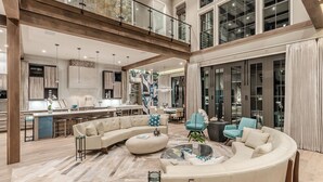 A spacious living area with a curved sofa, a coffee table, and a dining area with a kitchen in the background. - Vermillion Sunsets | Lakefront Architectural Gem-Pool/Hot Tub/New 6 Seat LSV (Santa Rosa Beach)