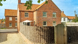 A brick house with a tiled roof, a wooden fence, and a gravel driveway.