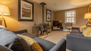 A cozy living room with a fireplace, two sofas, a TV, and framed pictures on the wall.
