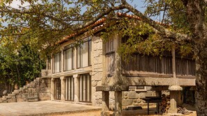A stone building with large windows, a stone bench, and a fire pit. - Casa da Eira - Casa Rural com Piscina Privada (Oliveira (São Pedro))