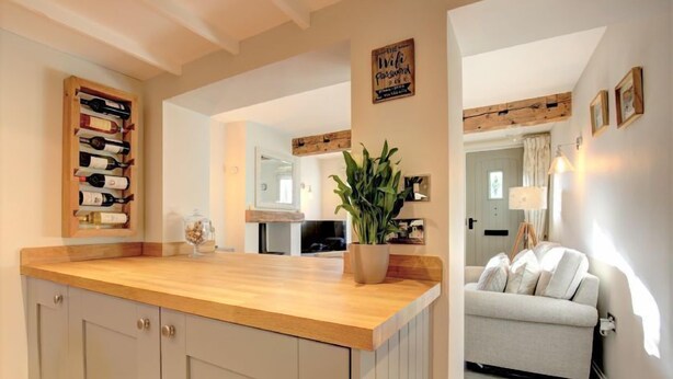 A kitchen with a wooden countertop, cabinets, and a wine rack. There is a plant on the countertop and a sofa in the adjacent living area. - Pond Cottage, Docking, Norfolk (Docking)